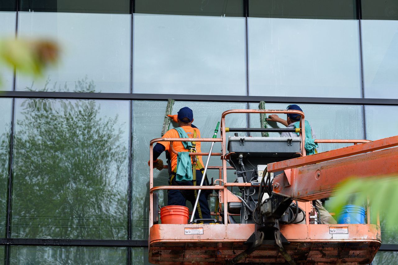 Deux opérateurs nettoient les vitres d’une façade en verre à l’aide d’une plateforme élévatrice, afin d’améliorer l’apparence du bâtiment.